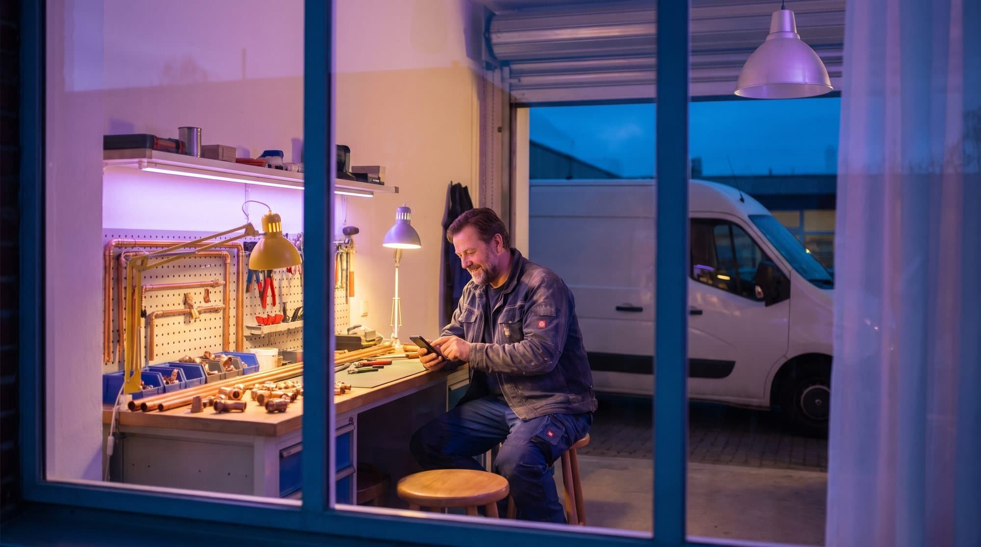 VVS-mester tjekker sin telefon i værkstedet ved fyraften, den hvide varevogn holder udenfor