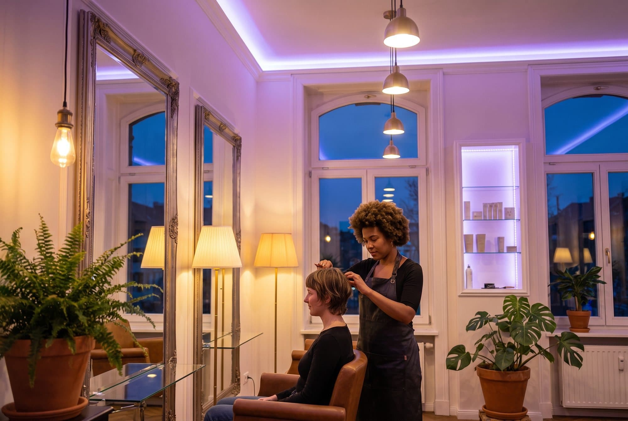 Frisør klipper en kunde i en salon med høje buede vinduer